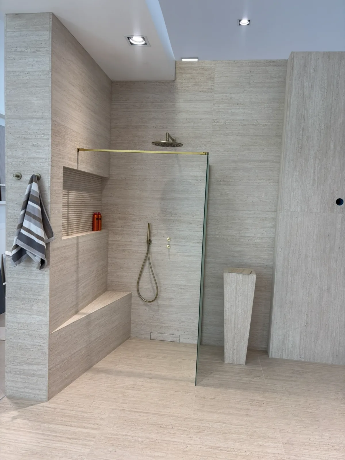 Douche à l'italienne tout en carrelage grand format effet travertin, avec banc intégré.